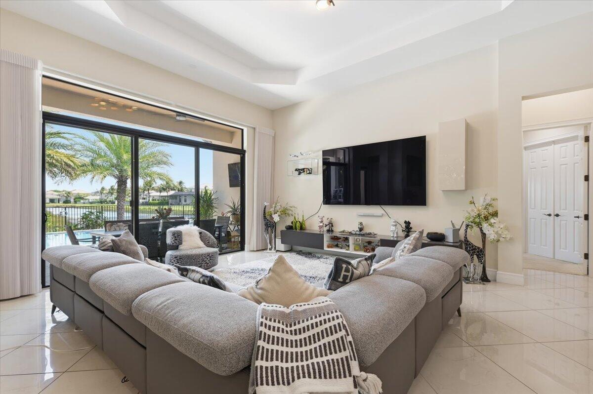 A living room features a large gray sectional sofa, a wall-mounted television, and sliding glass doors — 9769 Bozzano Drive, Delray Beach FL 33446, DELRAY BEACH, FL
