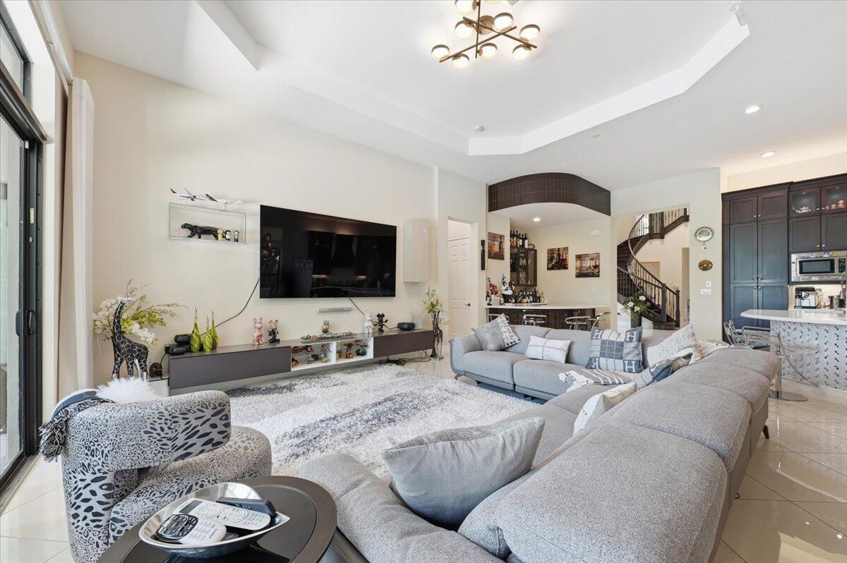 A spacious living room features a large sectional sofa, a wall-mounted television, and tile flooring — 9769 Bozzano Drive, Delray Beach FL 33446, DELRAY BEACH, FL