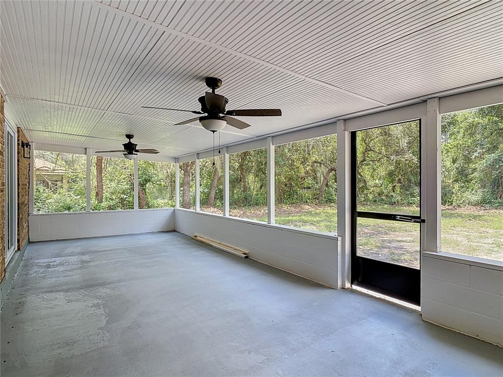 A screened-in porch features a concrete floor, two ceiling fans, and white paneled walls — 1483 TIVOLI DRIVE, DELTONA, FL