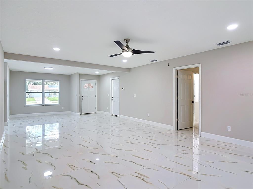 A spacious room features white marble-look tile flooring, light gray walls, and a ceiling fan — 1483 TIVOLI DRIVE, DELTONA, FL