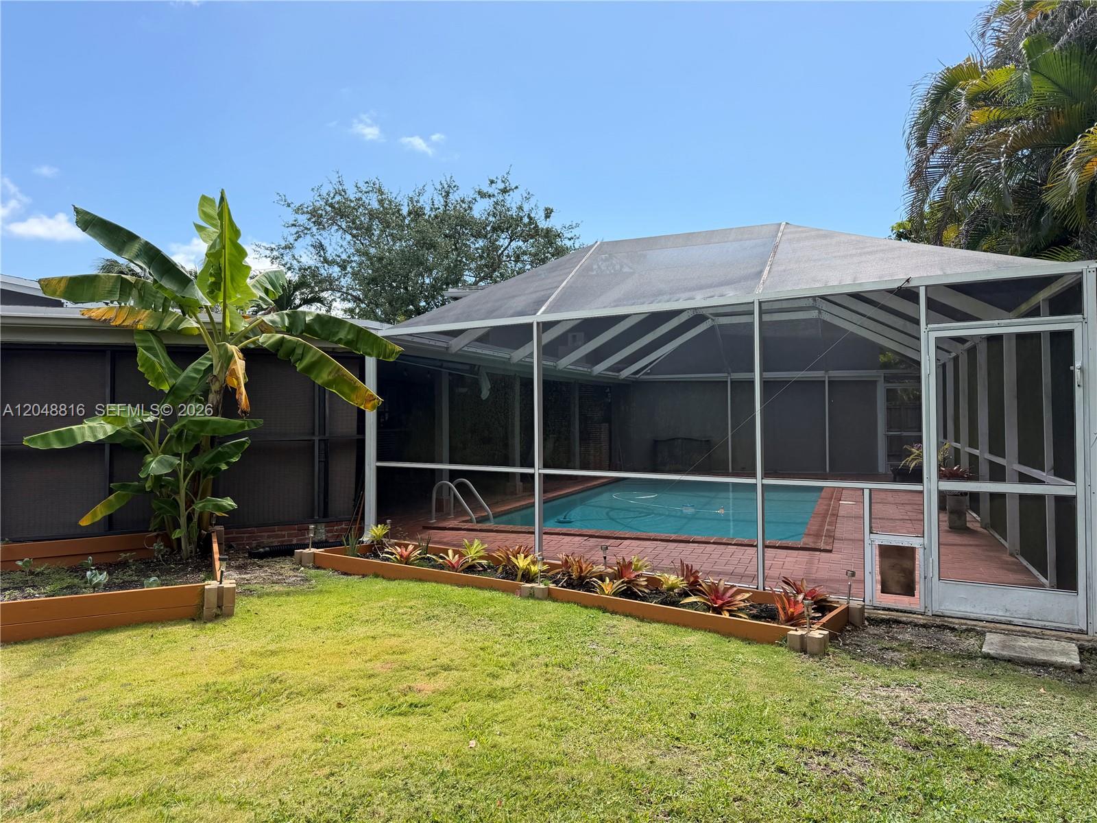 A backyard features a screened-in swimming pool, a banana tree, and raised garden beds — 13200 SW 83rd Ave, Pinecrest FL 33156, PINECREST, FL
