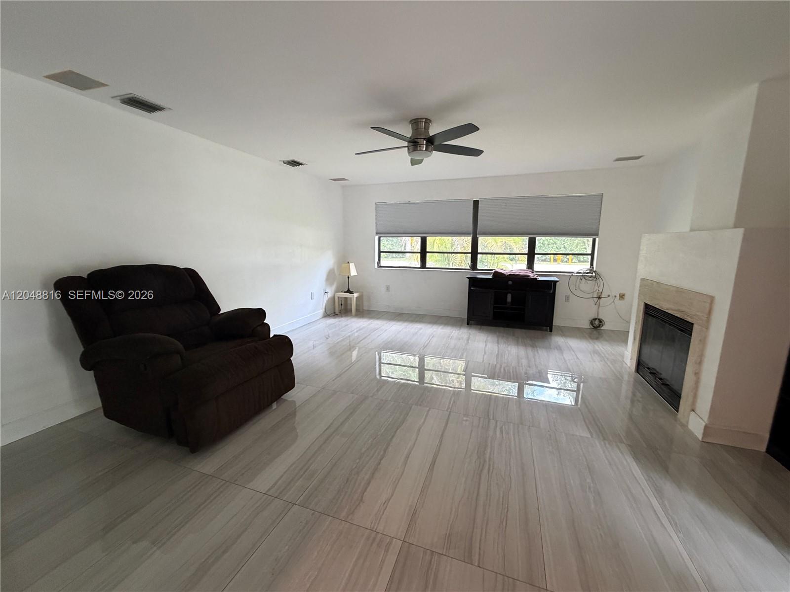 A living room features a dark recliner, a fireplace, and light-colored tile flooring — 13200 SW 83rd Ave, Pinecrest FL 33156, PINECREST, FL