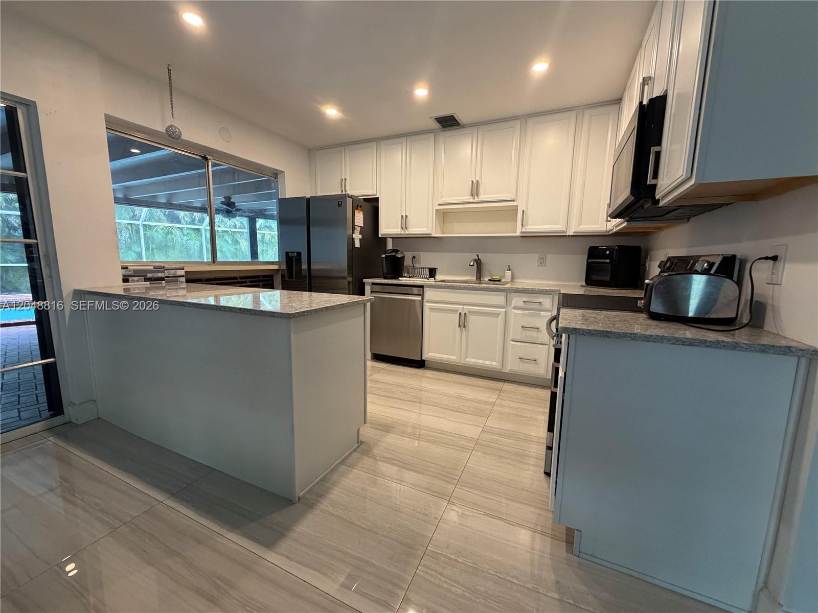 A kitchen features white cabinets, stainless steel appliances, granite countertops, and light-colored tile flooring — 13200 SW 83rd Ave, Pinecrest FL 33156, PINECREST, FL