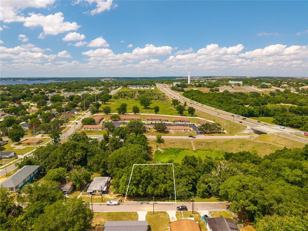 An aerial view shows a vacant, tree-covered lot outlined in white along a residential street — E MINNEOLA AVENUE, CLERMONT, FL