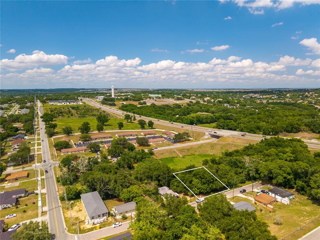 An aerial view shows a vacant, tree-covered lot outlined in white near a highway — E MINNEOLA AVENUE, CLERMONT, FL