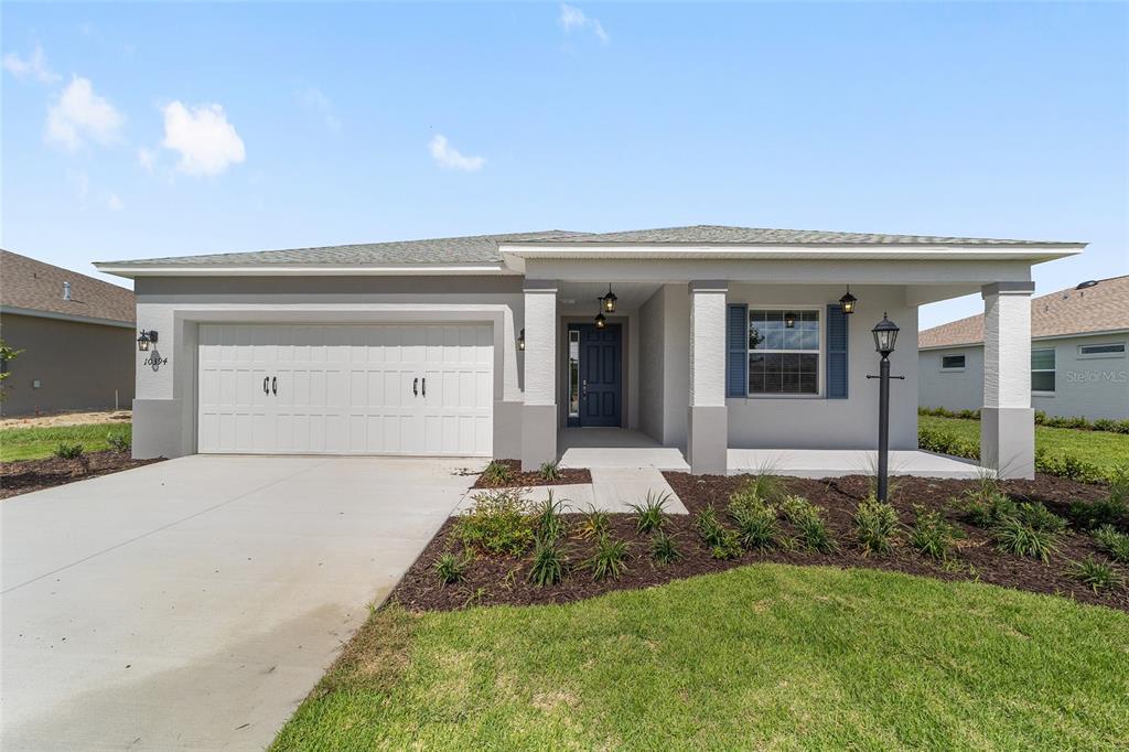 A single-story house with a white garage, gray stucco exterior, and a covered front porch — 10394 SW 107TH COURT, OCALA, FL