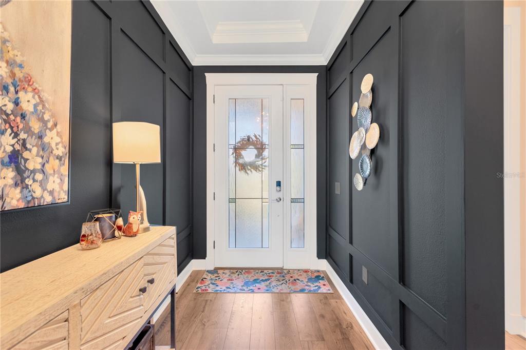 A foyer features dark paneled walls, a light wood console table, and a glass-paneled front door — 7213 TALAMORE DRIVE, WESLEY CHAPEL, FL
