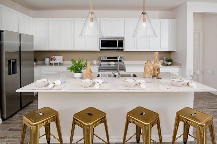 A modern kitchen features white cabinets, a large island with gold stools, and stainless appliances — 2029 ANTHEM DRIVE, ORANGE CITY, FL
