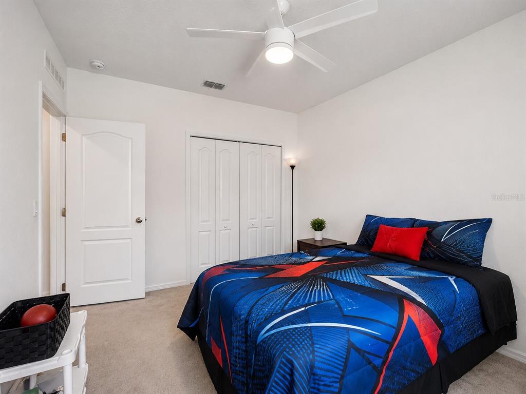 A bedroom features a bed with a blue and red patterned comforter and carpeted flooring — 626 GILA DRIVE, POINCIANA, FL