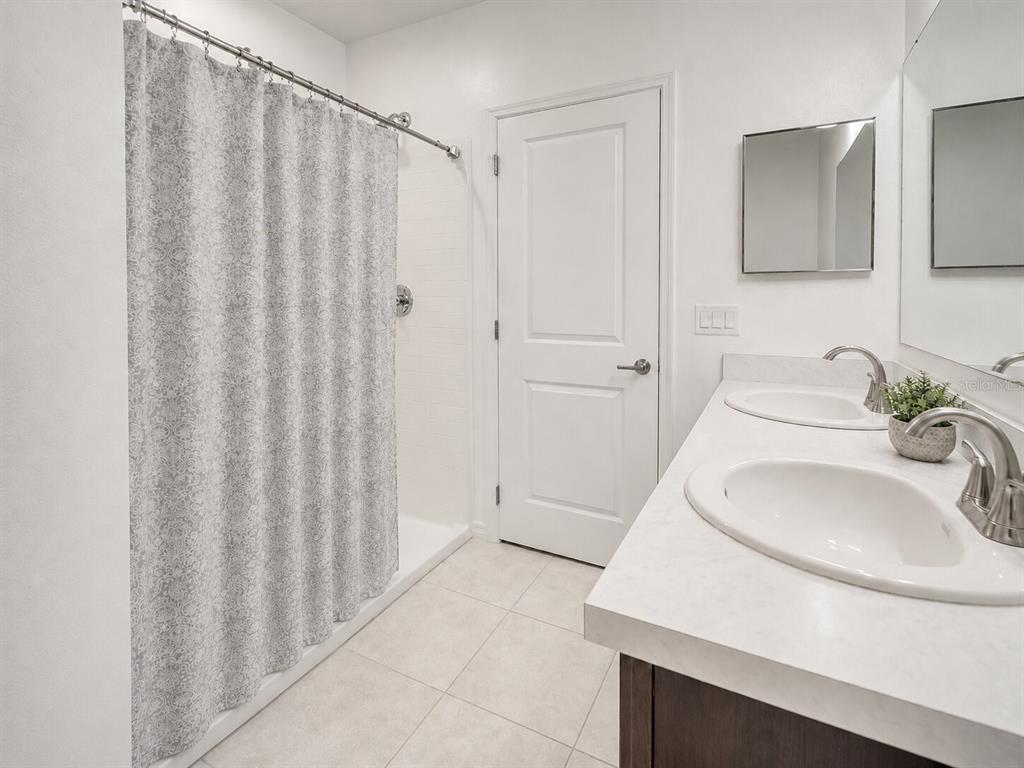 A bathroom features a double vanity with white countertops, a walk-in shower, and a closed door — 626 GILA DRIVE, POINCIANA, FL