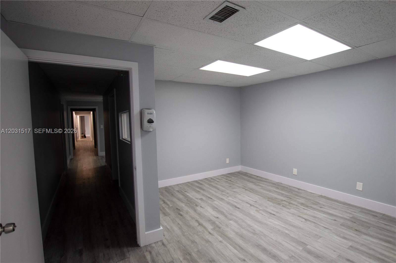 An empty office room features gray walls, light wood-look flooring, and a drop ceiling — HOLLYWOOD, FL
