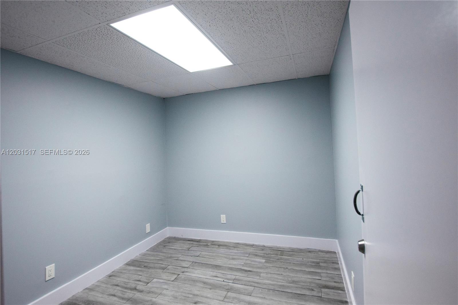 An empty room features light blue walls, wood-look tile flooring, and a drop ceiling — HOLLYWOOD, FL