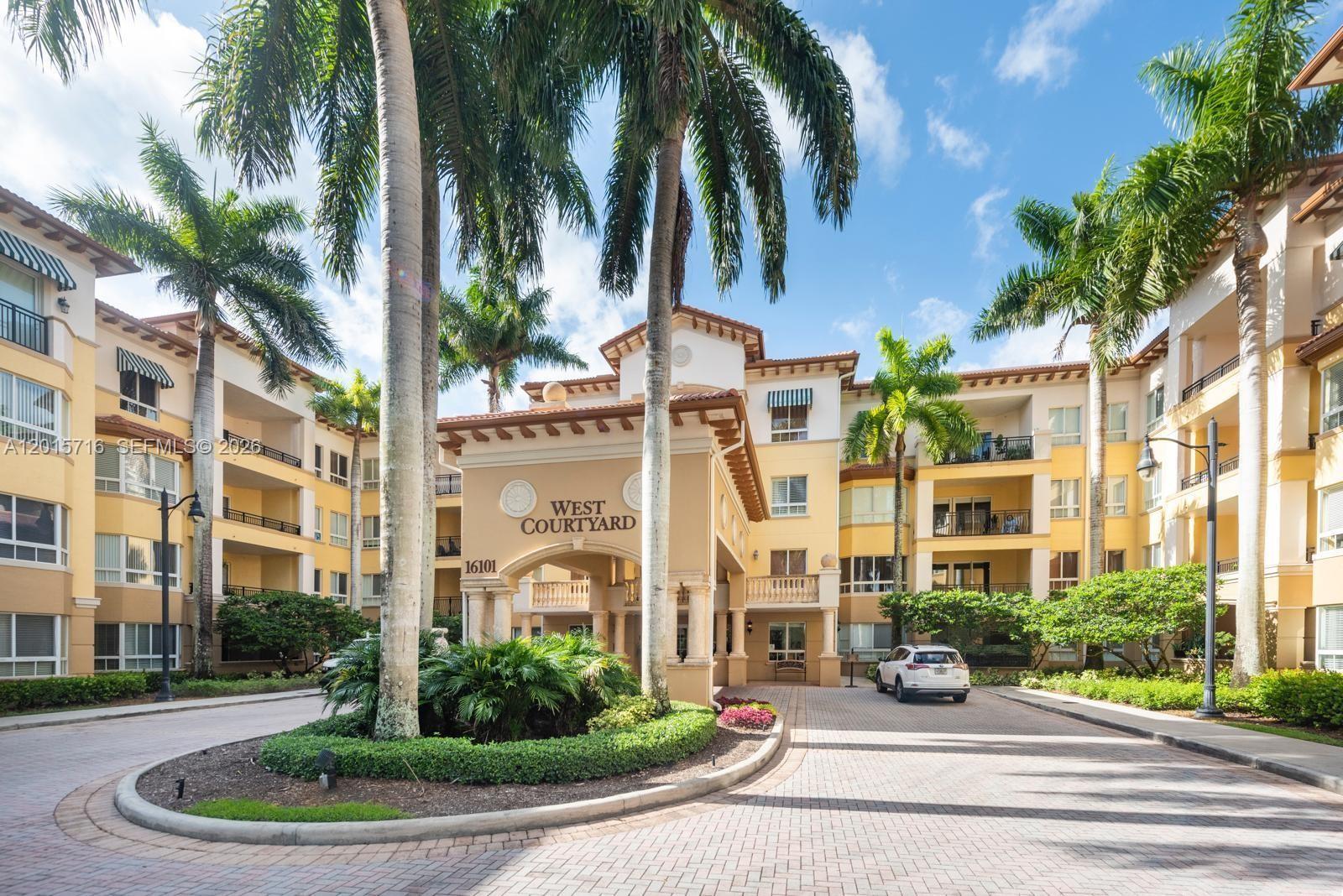 A paved driveway leads to the entrance of a multi-story apartment building with palm trees — 16101 Emerald Estates Dr # 254, Weston FL 33331, WESTON, FL