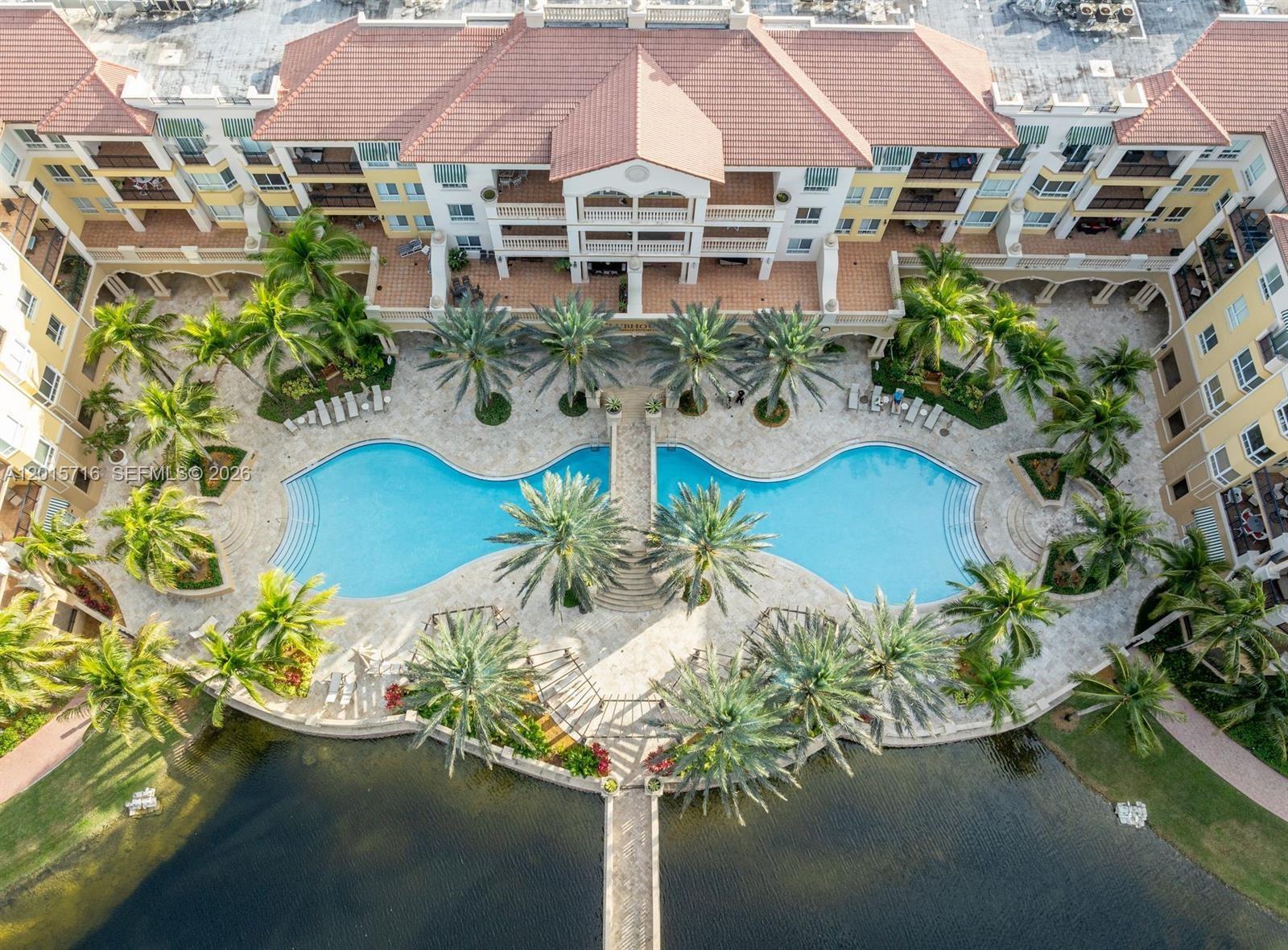 An aerial view shows a large swimming pool with a bridge between two apartment buildings — 16101 Emerald Estates Dr # 254, Weston FL 33331, WESTON, FL