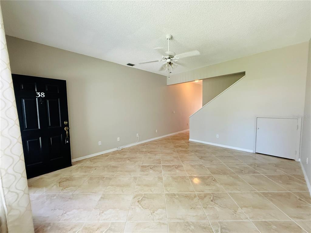 An interior view shows a room with beige tile flooring, a black front door, and a staircase — 2843 THAXTON DRIVE UNIT 38, PALM HARBOR, FL