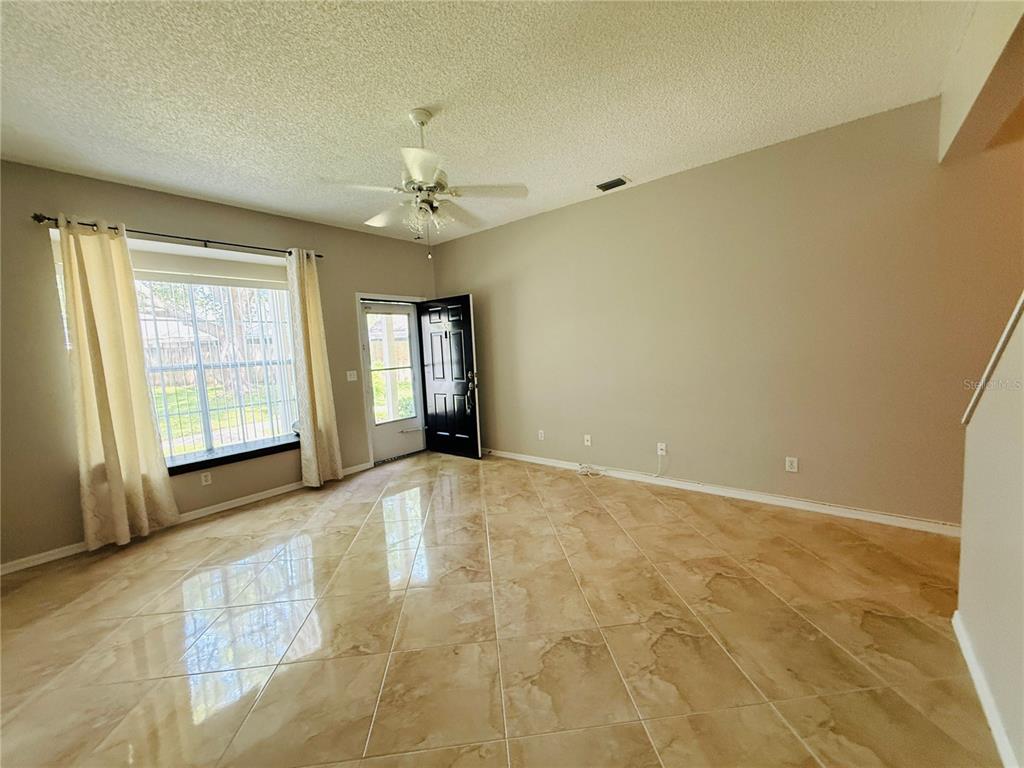 A living room with beige tile flooring, a ceiling fan, and a large bay window — 2843 THAXTON DRIVE UNIT 38, PALM HARBOR, FL