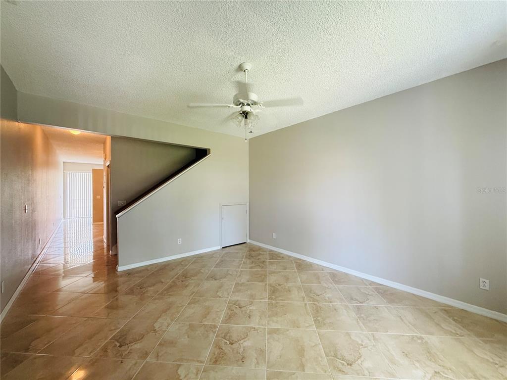 An empty room with beige tile flooring, a ceiling fan, and a staircase wall — 2843 THAXTON DRIVE UNIT 38, PALM HARBOR, FL