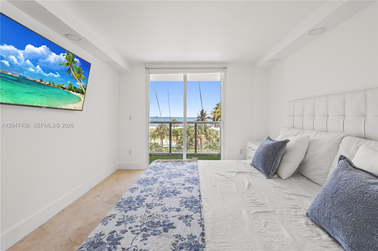 A bedroom features a white tufted headboard, a floral bedspread, and a balcony with ocean views — 2457 Collins Ave # 406, Miami Beach FL 33140, MIAMI BEACH, FL