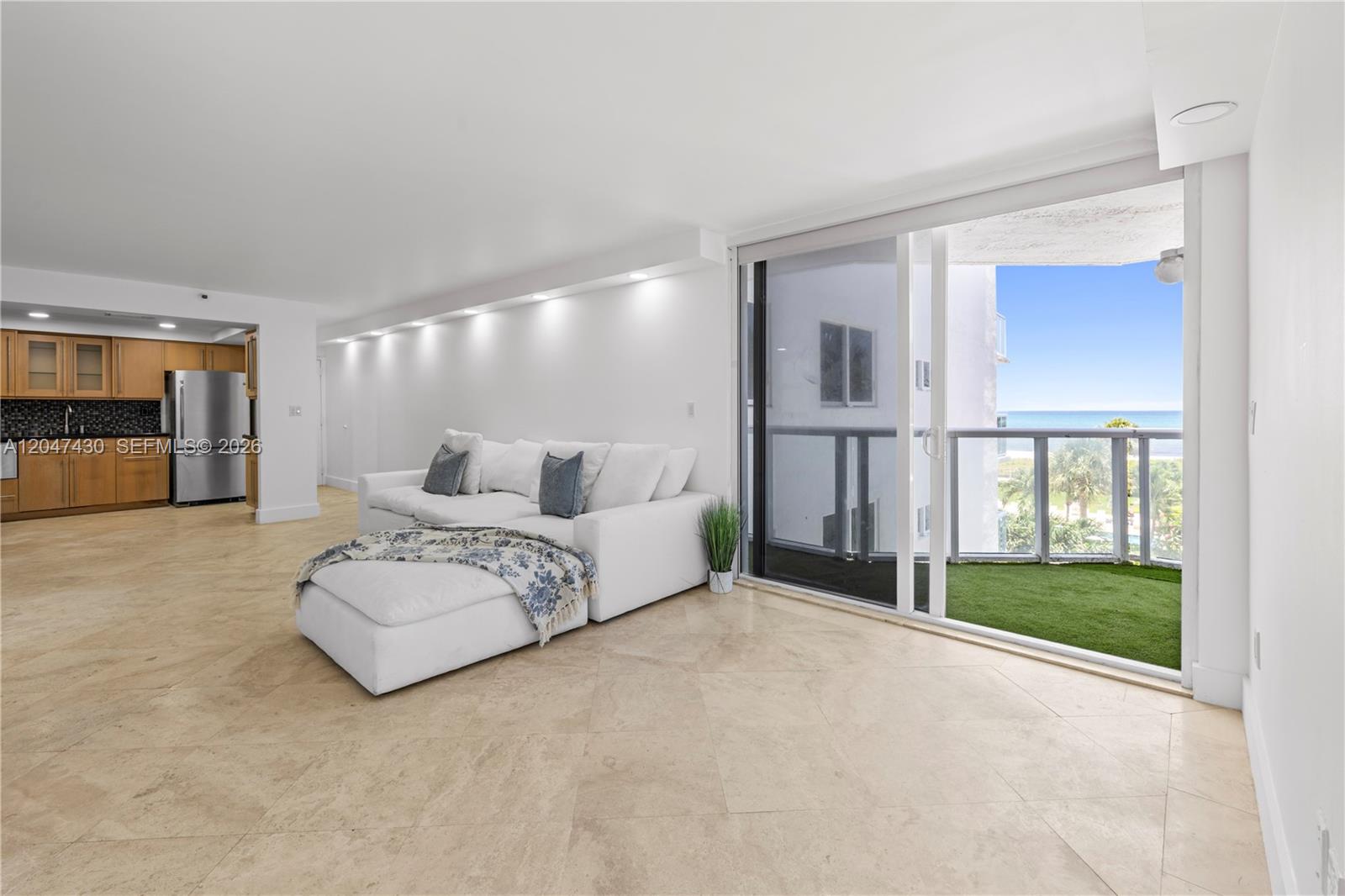 A living room with a white sectional sofa, tile floors, and a balcony overlooking the ocean — 2457 Collins Ave # 406, Miami Beach FL 33140, MIAMI BEACH, FL