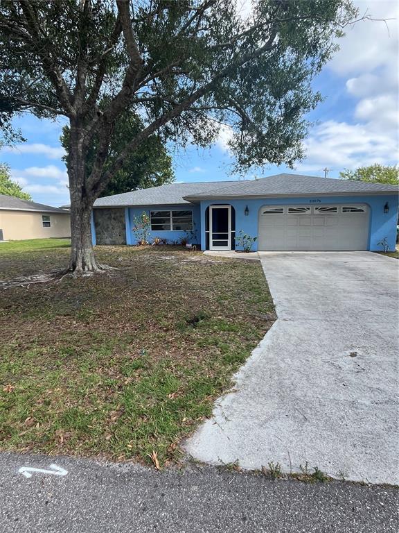 A blue single-story house with a two-car garage and a large tree in the yard — 23076 AUGUST AVENUE, PORT CHARLOTTE, FL