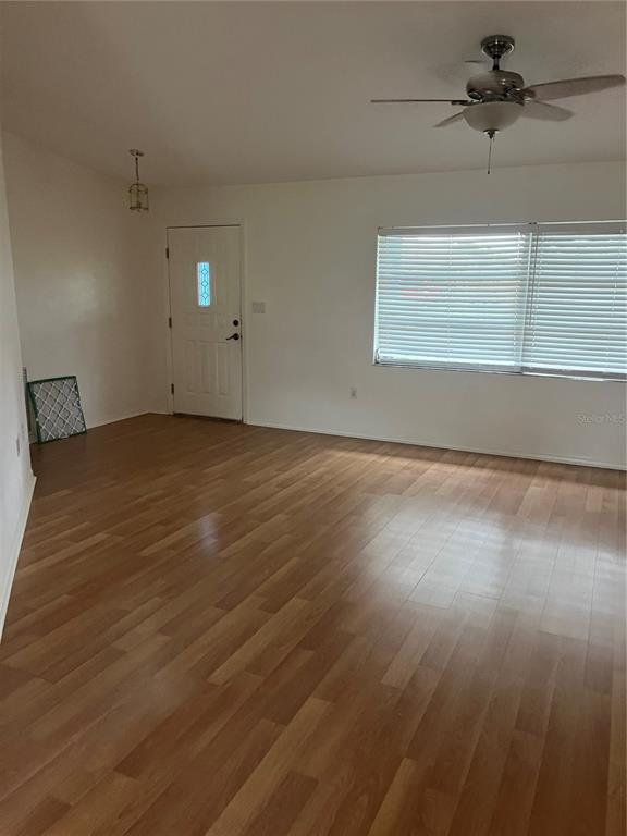 An empty room features light wood-look flooring, white walls, a ceiling fan, and a door — 23076 AUGUST AVENUE, PORT CHARLOTTE, FL