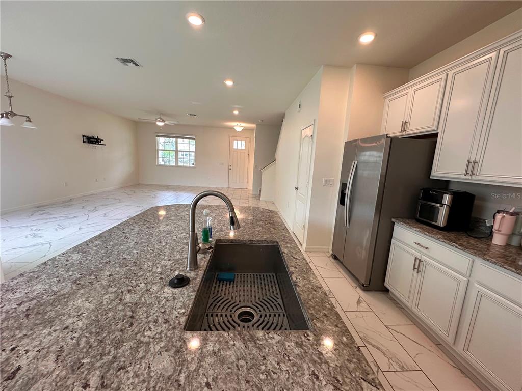 A kitchen island with a stainless steel sink overlooks an open-concept living area with tile floors — 5844 SOTER LANE, WINDERMERE, FL
