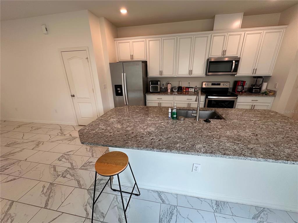 A kitchen features white cabinets, granite countertops, a large island, and light-colored marble-patterned tile flooring — 5844 SOTER LANE, WINDERMERE, FL