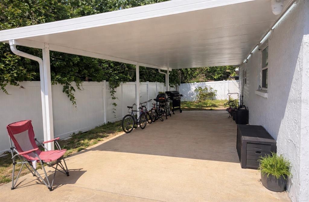 A concrete patio with a white metal roof cover, bicycles, a grill, and a chair — 5338 TROUBLE CREEK ROAD, NEW PORT RICHEY, FL