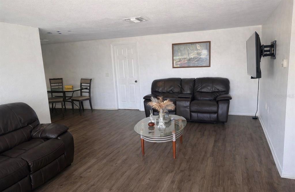 A living room with dark leather sofas, a glass coffee table, and wood-look flooring — 5338 TROUBLE CREEK ROAD, NEW PORT RICHEY, FL
