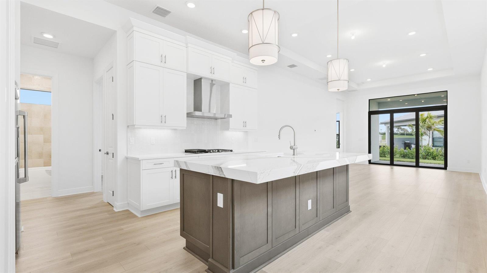 A modern kitchen features white cabinetry, a gray island with marble countertops, and light flooring — 5084 Lido Key Lane, Westlake FL 33470, WESTLAKE, FL