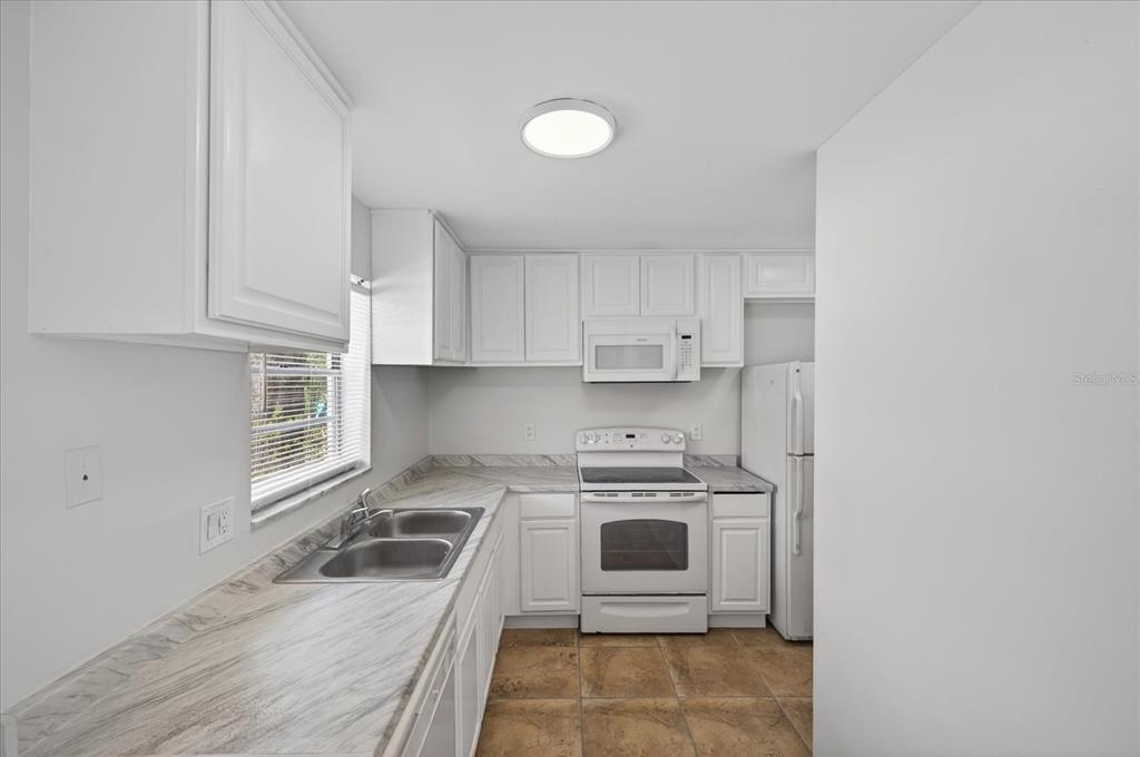A kitchen with white cabinets, marble-patterned countertops, white appliances, and tan tile flooring — 14024 VILLAGE TERRACE DRIVE, TAMPA, FL