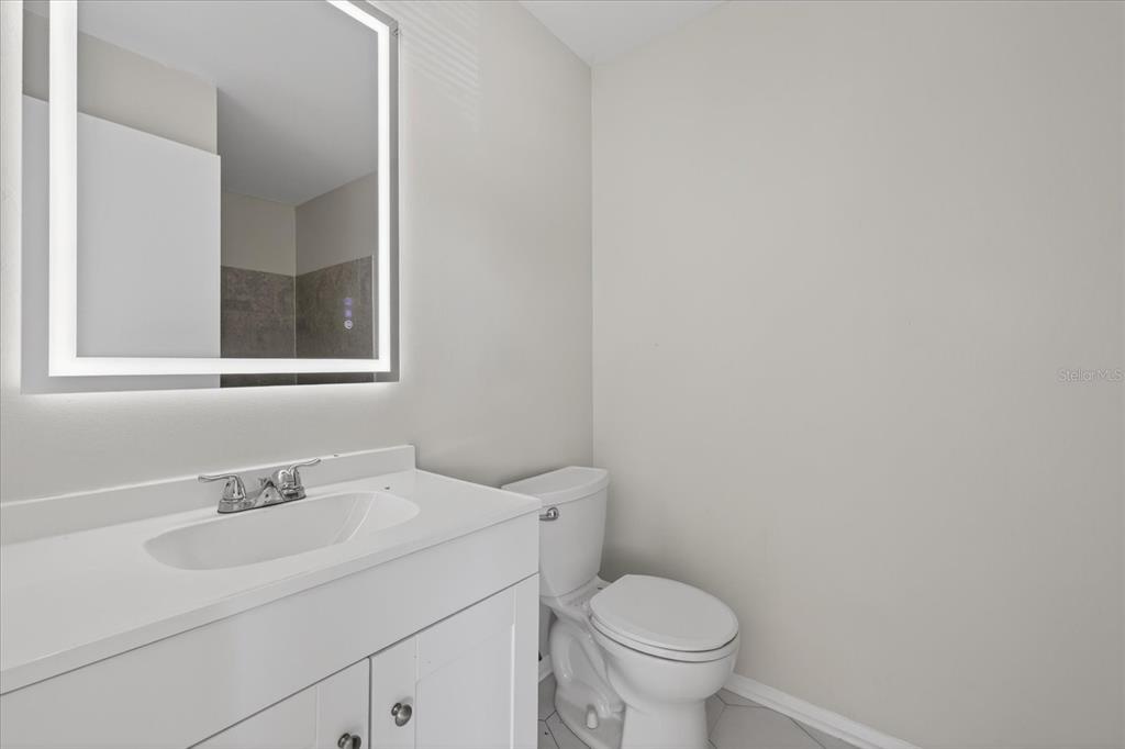 A bathroom features a white vanity with a sink, a lighted mirror, and a toilet — 14024 VILLAGE TERRACE DRIVE, TAMPA, FL