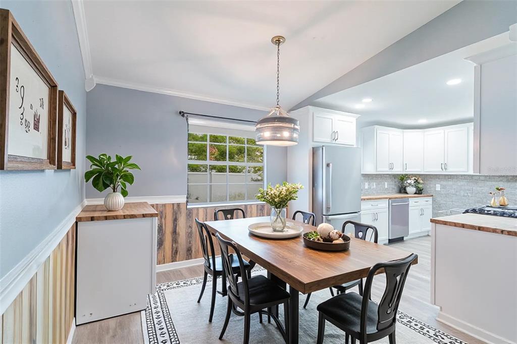 A dining area with a wooden table, black chairs, and wood-paneled walls next to a kitchen — 109 REBECCA DRIVE NE, WINTER HAVEN, FL