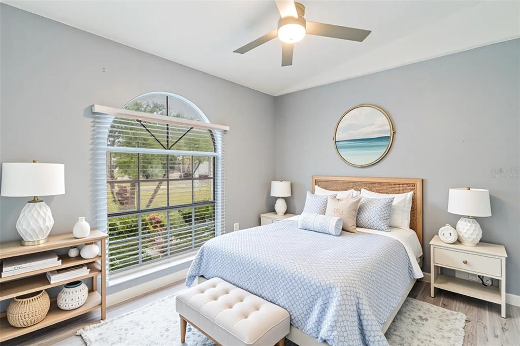 A bedroom features a queen bed, arched window, ceiling fan, and light-colored wood furniture — 109 REBECCA DRIVE NE, WINTER HAVEN, FL