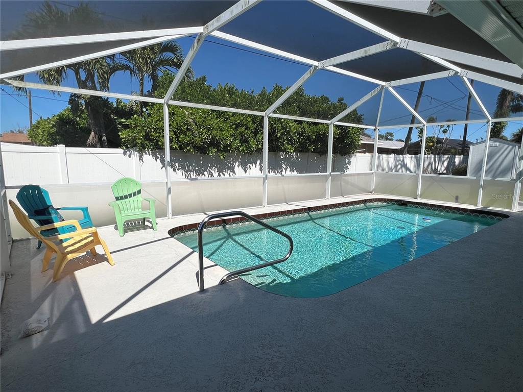 A rectangular swimming pool is enclosed by a screened lanai with three outdoor chairs — 1536 PORPOISE ROAD, VENICE, FL