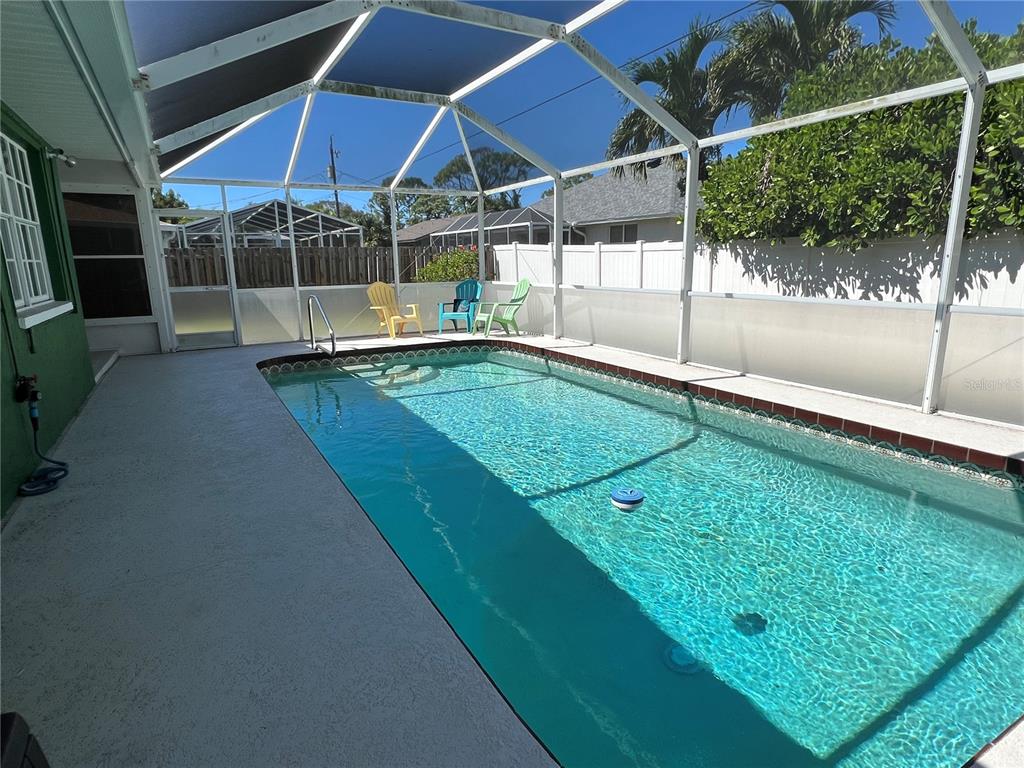 A rectangular swimming pool is enclosed by a screened lanai with three colorful chairs — 1536 PORPOISE ROAD, VENICE, FL