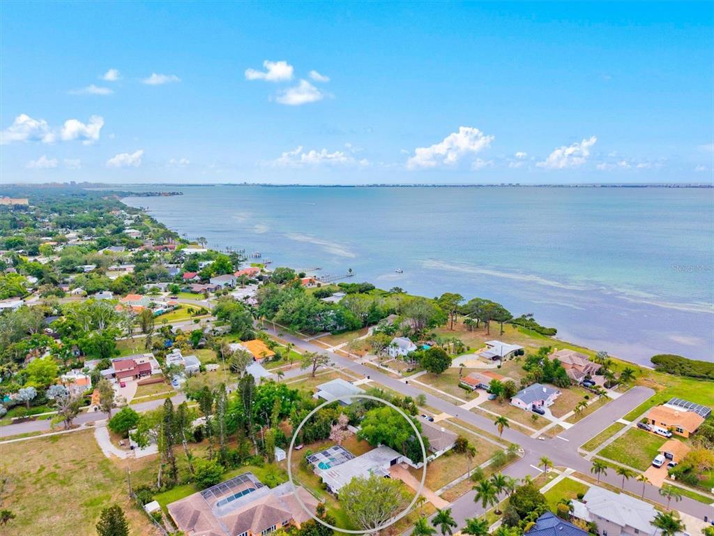 An aerial view shows a residential house with a pool enclosure circled near the waterfront — 214 GAINES AVENUE, SARASOTA, FL