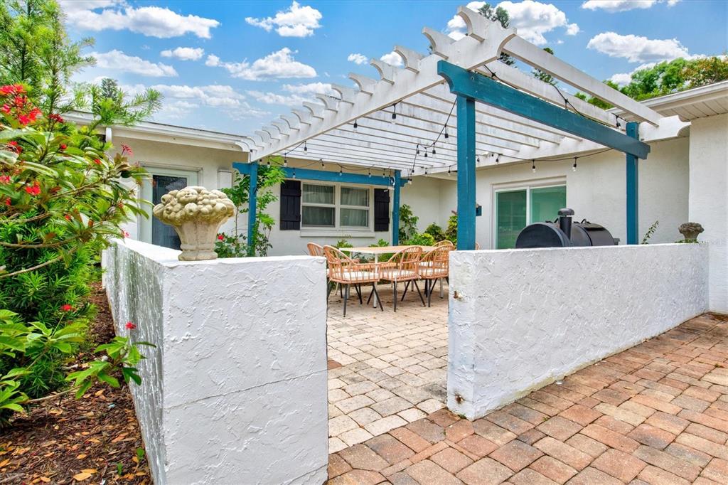 A patio features a white pergola, string lights, a dining set, and a low wall — 214 GAINES AVENUE, SARASOTA, FL