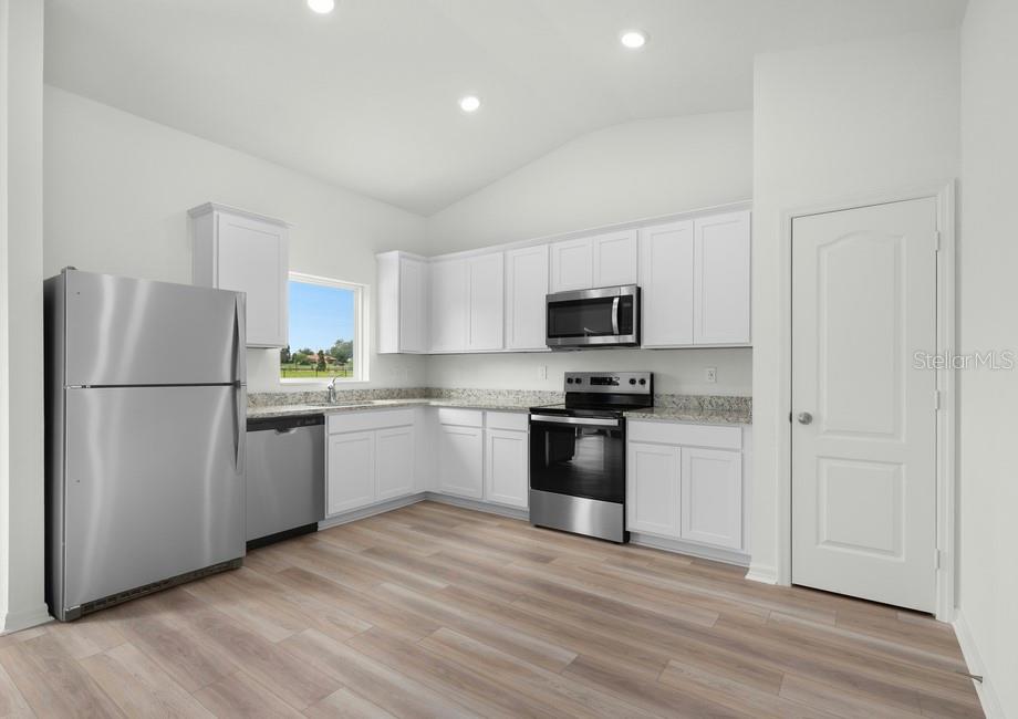 A kitchen with white cabinets, stainless steel appliances, granite countertops, and light wood-look flooring — 632 TANGELO TERRACE, BABSON PARK, FL