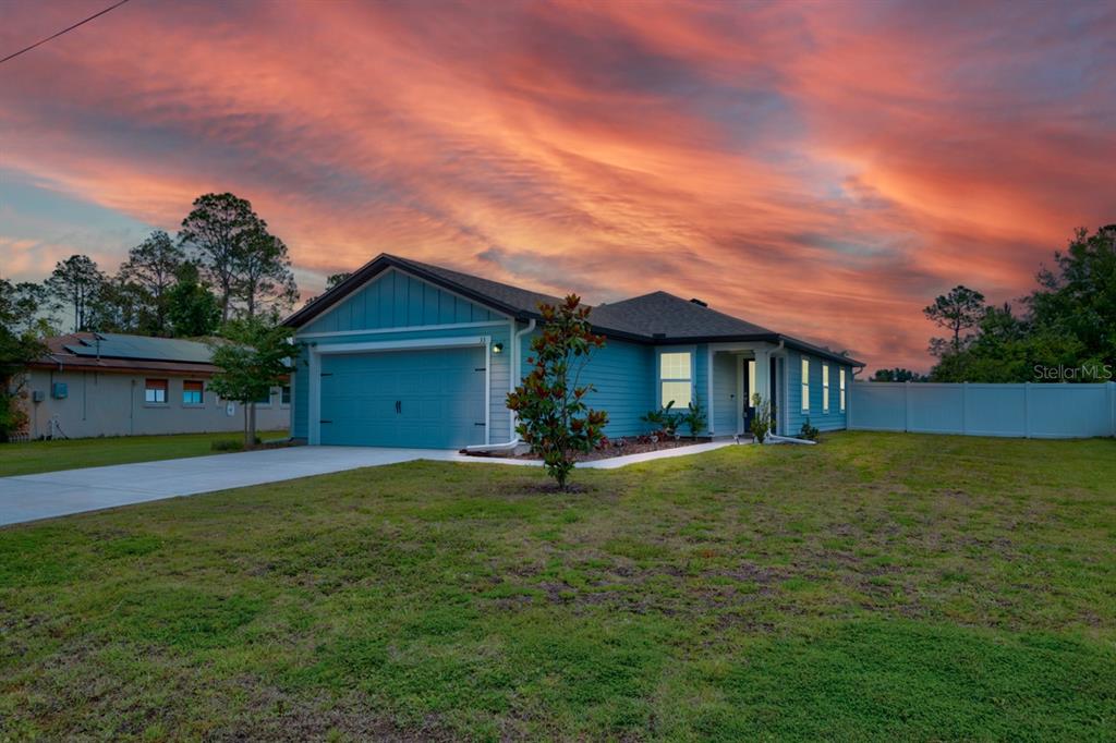 A blue single-story house with a two-car garage sits on a lawn at sunset — 33 PINE CROFT LANE, PALM COAST, FL