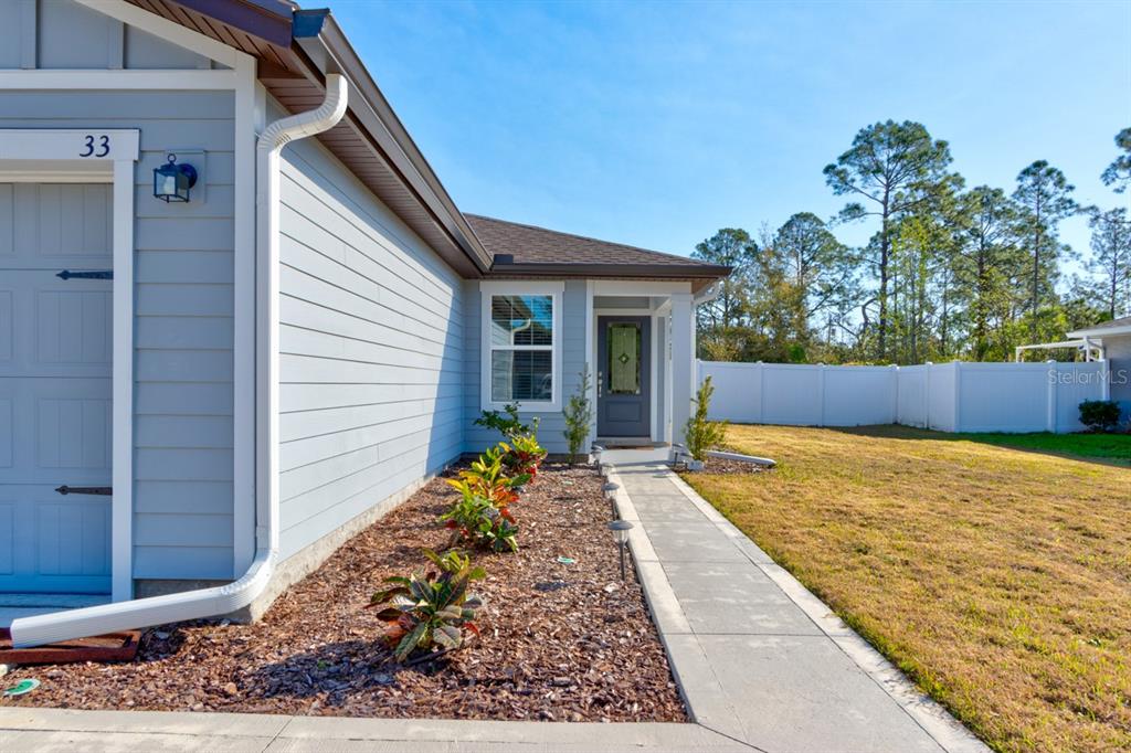 A light blue house exterior features a walkway leading to the front door and landscaping — 33 PINE CROFT LANE, PALM COAST, FL