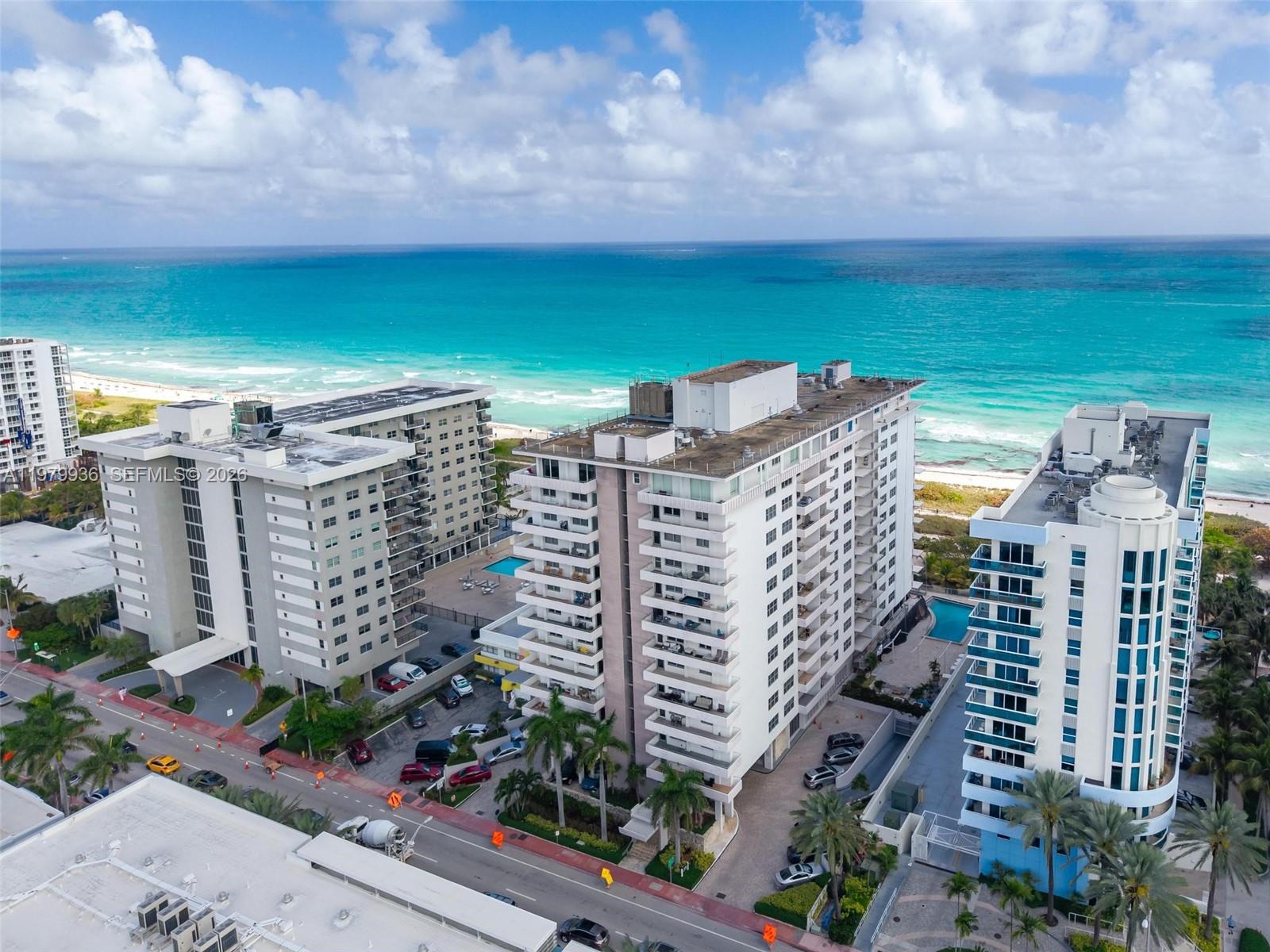 An aerial view shows three high-rise residential buildings situated along a sandy beach and ocean — 9225 Collins Ave # 610, Surfside FL 33154, SURFSIDE, FL