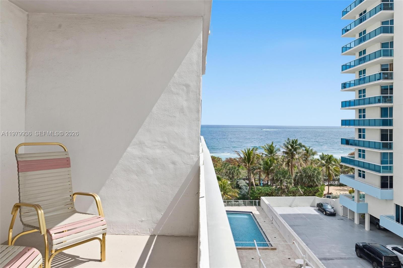 A balcony with a chair overlooks a swimming pool, a parking lot, and the ocean — 9225 Collins Ave # 610, Surfside FL 33154, SURFSIDE, FL