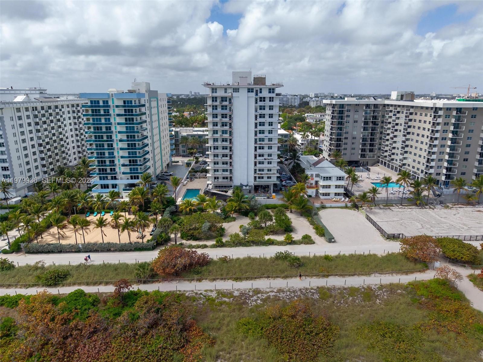 An aerial view shows several high-rise apartment buildings situated near a sandy beach and vegetation — 9225 Collins Ave # 610, Surfside FL 33154, SURFSIDE, FL