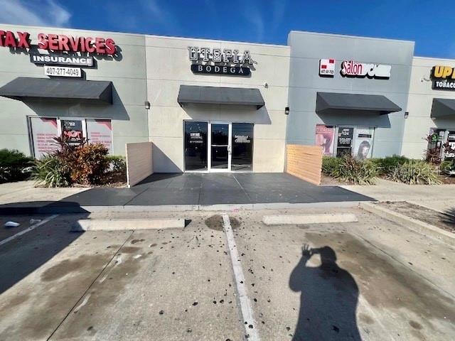 The exterior of a commercial strip mall features a central bodega storefront with flanking businesses — 3900 S GOLDENROD ROAD UNIT 118, ORLANDO, FL
