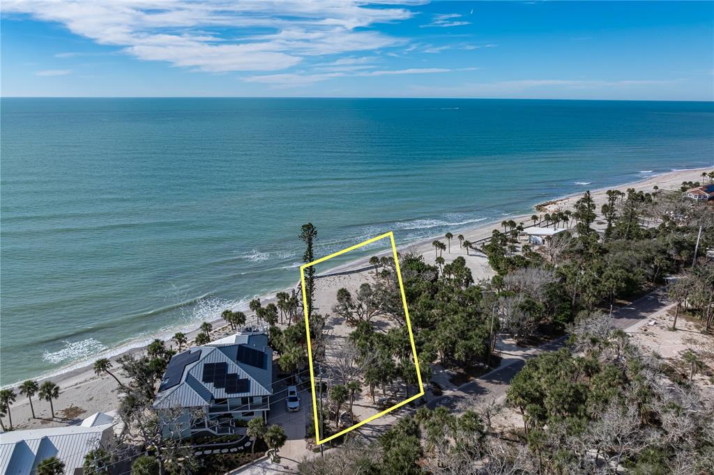 An aerial view shows a vacant, tree-covered beachfront lot outlined in yellow next to a house — 7210 MANASOTA KEY ROAD, ENGLEWOOD, FL