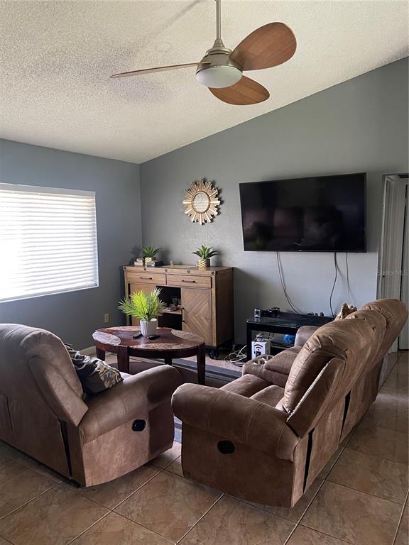 A living room features brown reclining furniture, a wooden cabinet, and a ceiling fan — 6801 COMPASS COURT, ORLANDO, FL