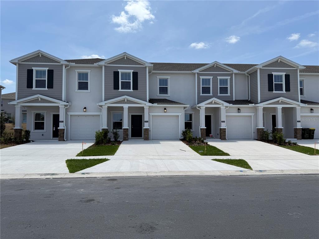 A row of four attached townhouses with gray siding, white trim, and individual garages — 2945 PROSPERITY WAY, CLERMONT, FL