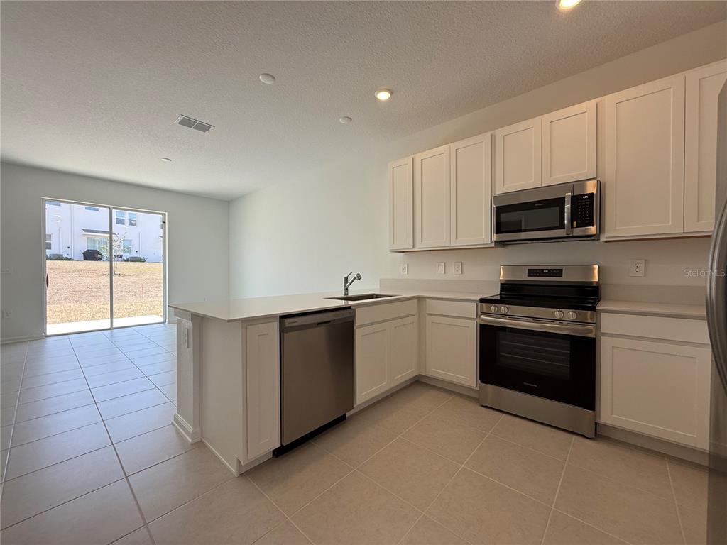 A kitchen with white cabinets, stainless steel appliances, and tile flooring leads to a patio — 2945 PROSPERITY WAY, CLERMONT, FL