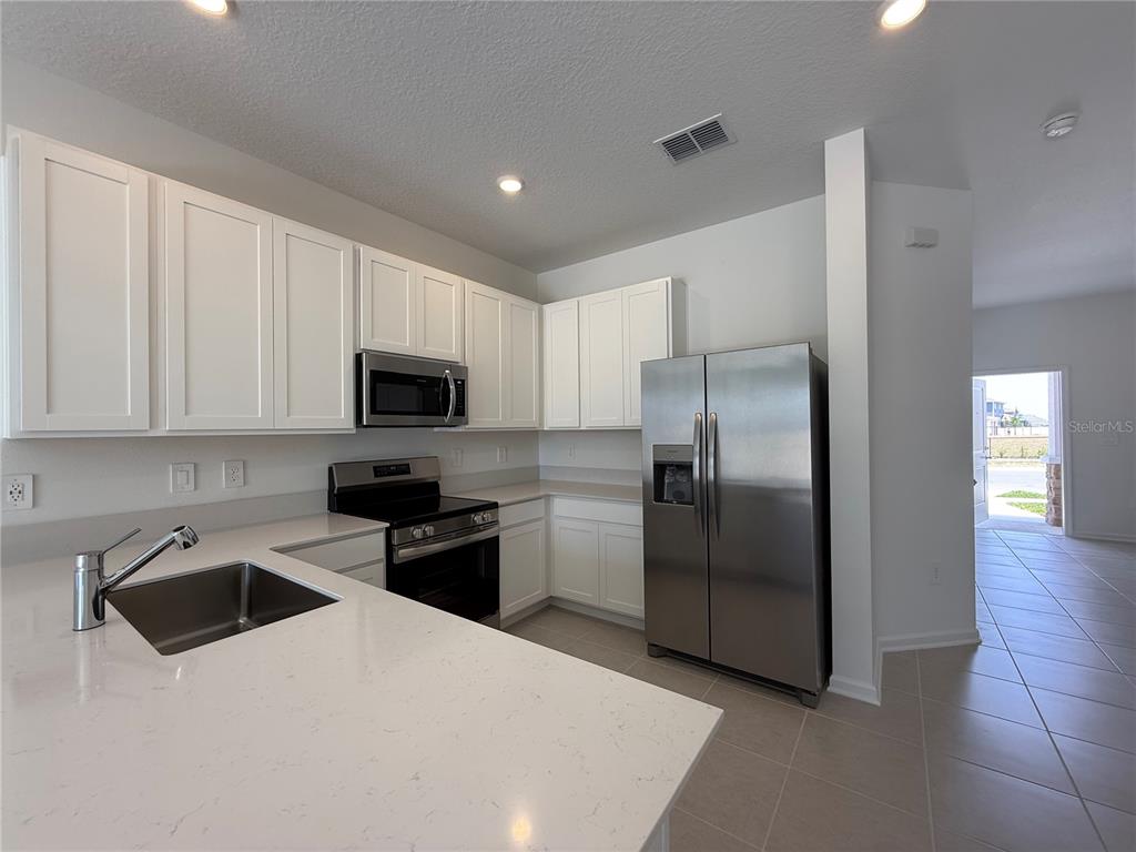 A kitchen features white cabinets, stainless steel appliances, and light-colored quartz countertops — 2945 PROSPERITY WAY, CLERMONT, FL